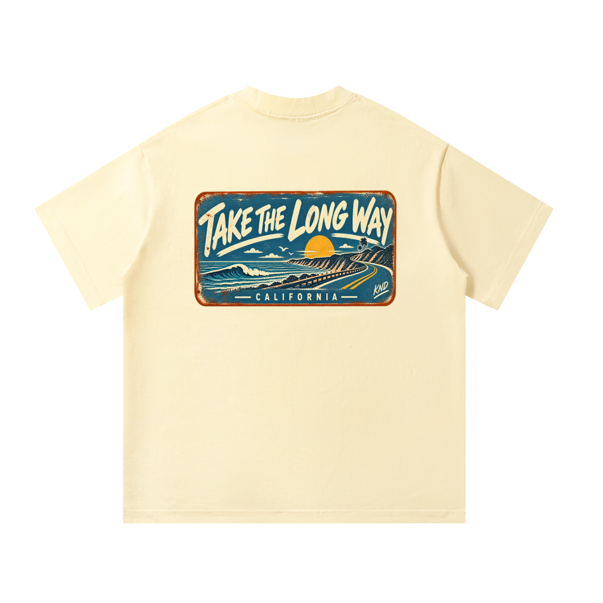 Take the Long Way Tee, Apricot — back print: a coast road winding along the cliffs at sunset past a breaking wave, in a weathered “Take the Long Way · California” sign
