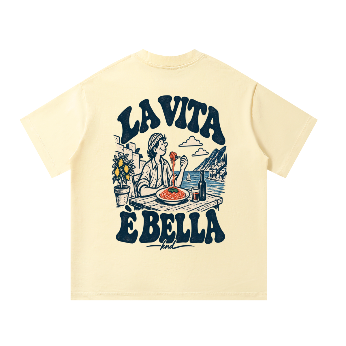 La Vita È Bella Tee, Apricot — back print: a man twirling spaghetti at a seaside table with a lemon tree and red wine, under “La Vita È Bella” lettering