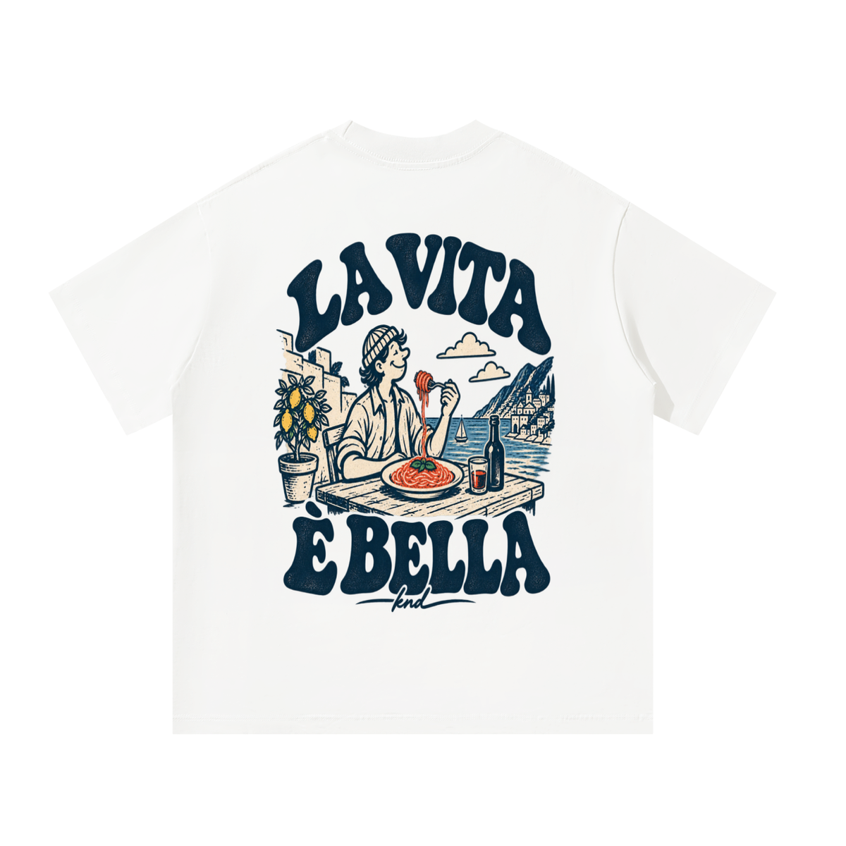 La Vita È Bella Tee, White — back print: a man twirling spaghetti at a seaside table with a lemon tree and red wine, under “La Vita È Bella” lettering