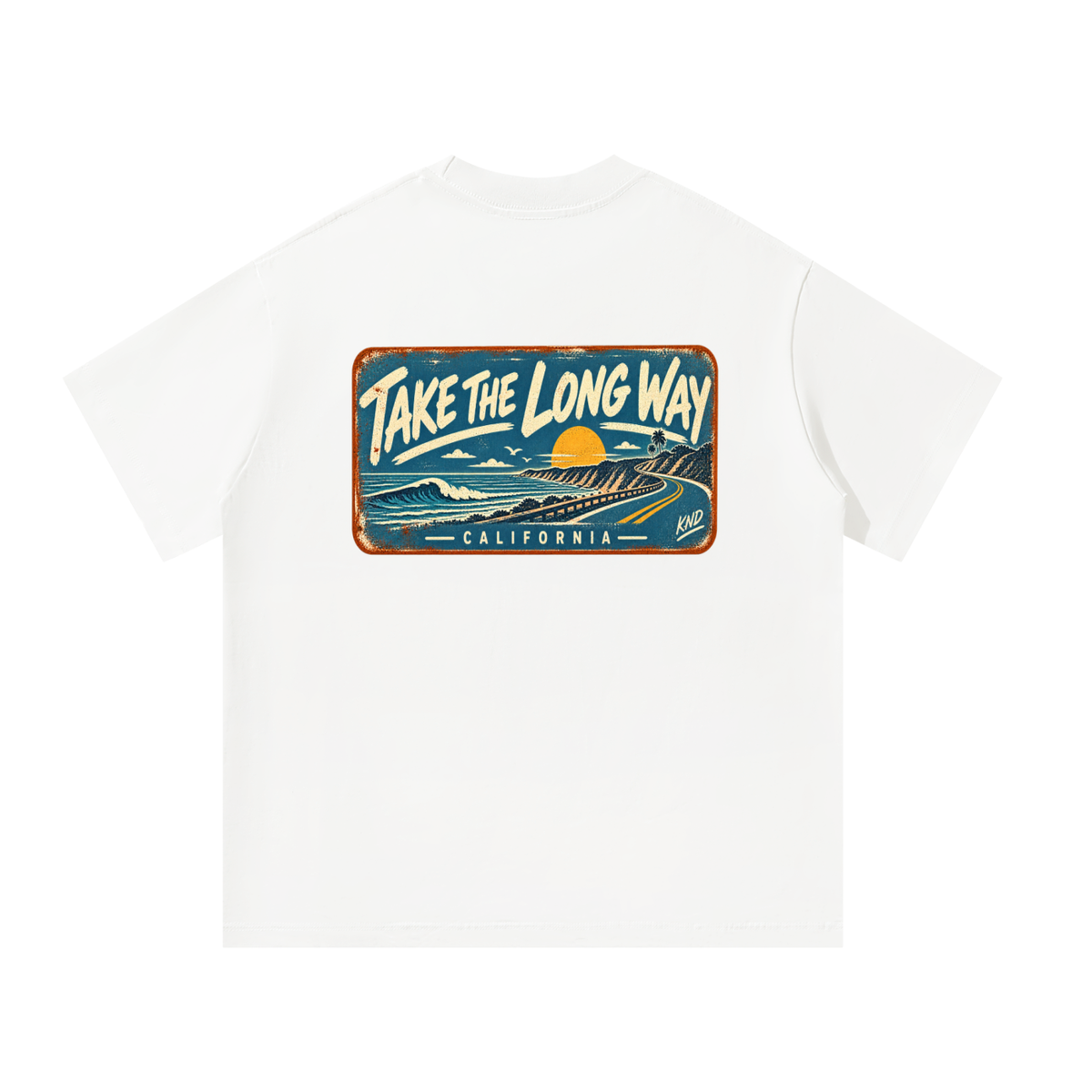 Take the Long Way Tee, White — back print: a coast road winding along the cliffs at sunset past a breaking wave, in a weathered “Take the Long Way · California” sign