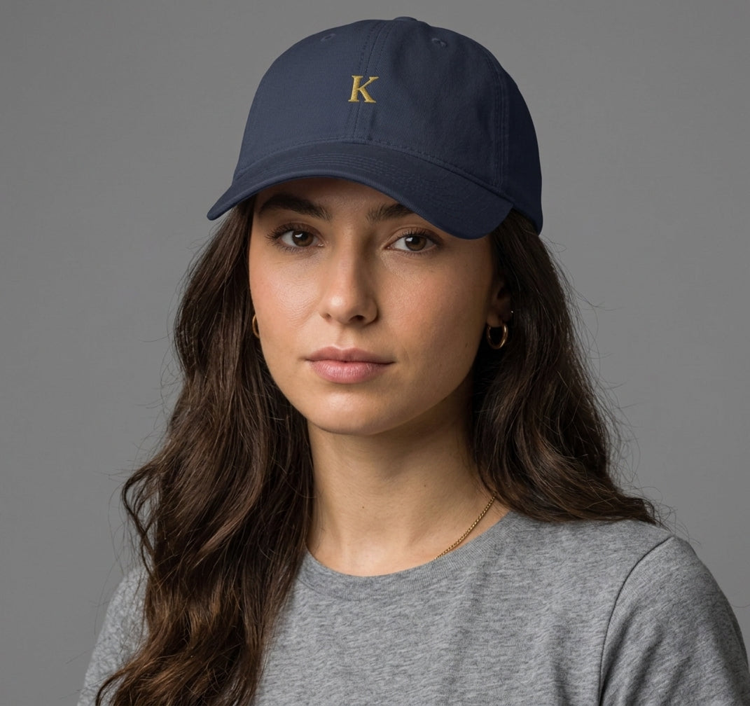 K Monogram Cap in navy — small gold K embroidered centre-front, pre-curved visor